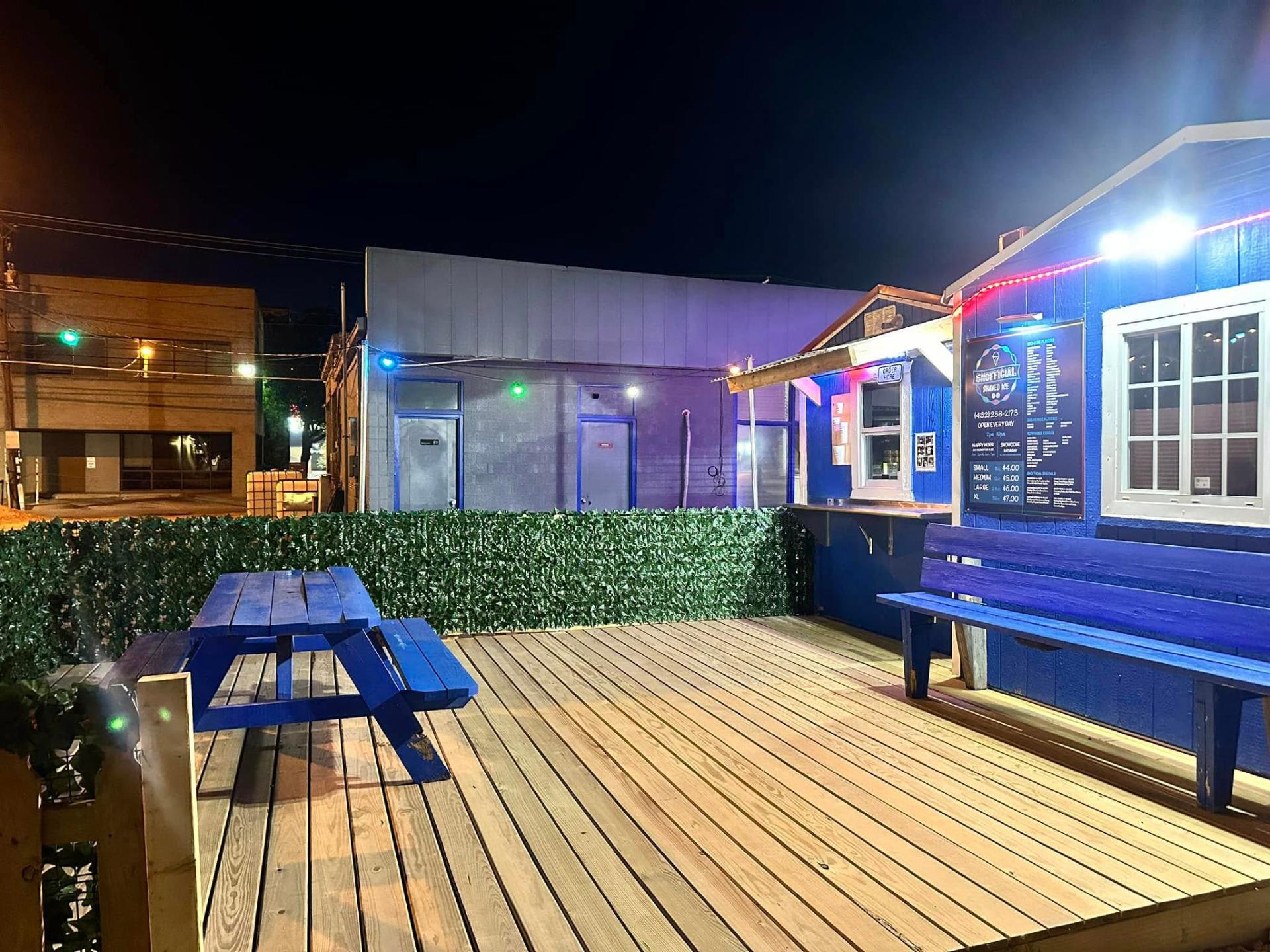 Snofficial Shaved Ice storefront at night with string lights and picnic tables